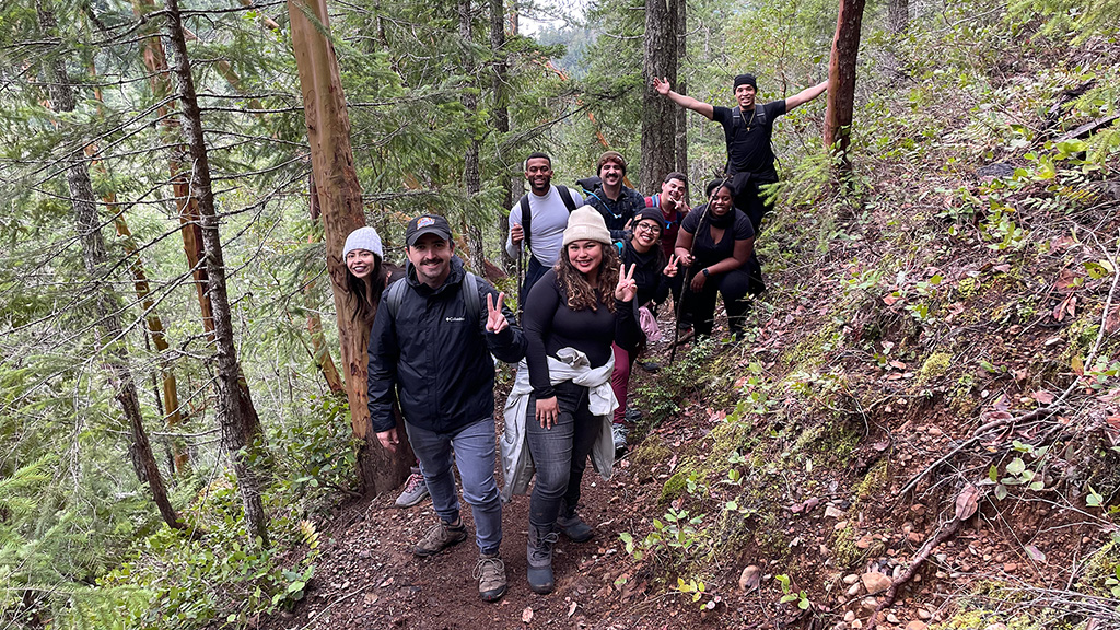 9 people pose for a group photo on a hillside trail in a forest